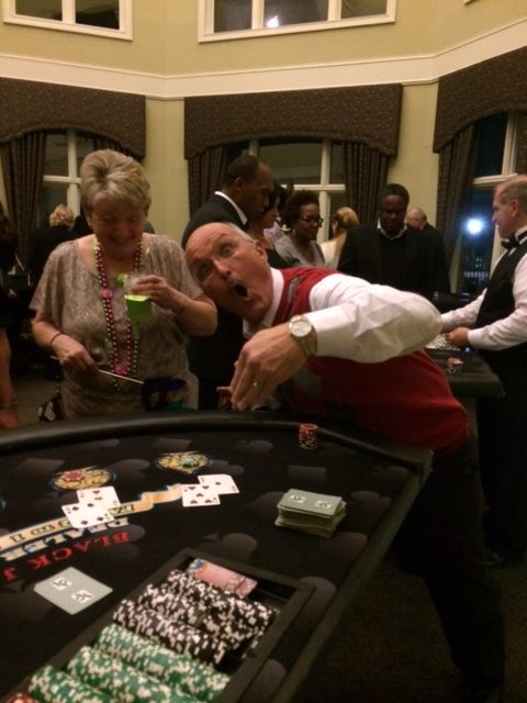 casino-party-guests-round-table - The Main Event Company Event guests gathering around a casino table