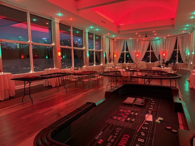 casino-tables-red-green-uplighting-windowed-venue - The Main Event Company Casino tables arranged in a window-lined room with red and green uplighting
