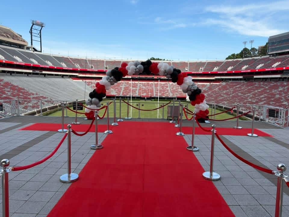 stadium-red-carpet-entrance-black-red-white-balloon-arch - The Main Event Company Red carpet entrance and balloon arch overlooking a football stadium